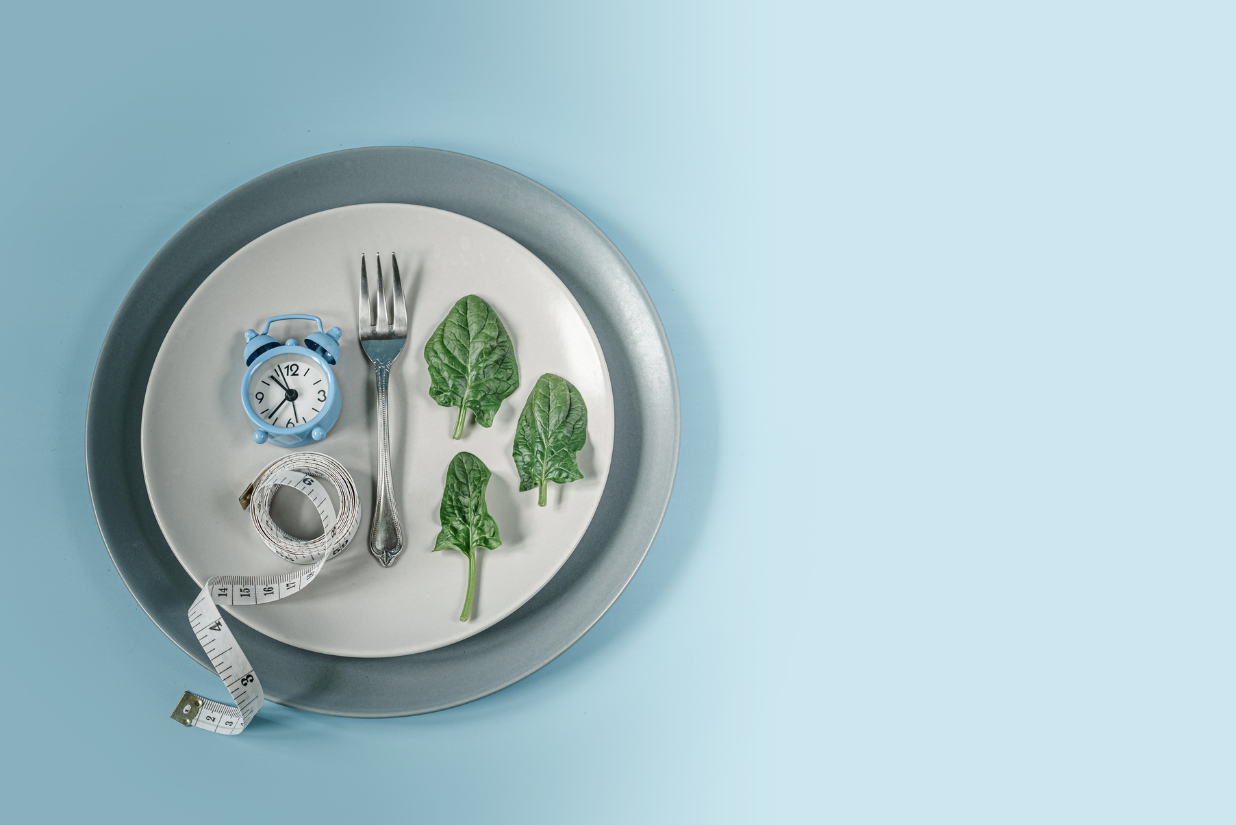 Clock, Fork, Spinach Leaves and Measure Tape on Gray Plate